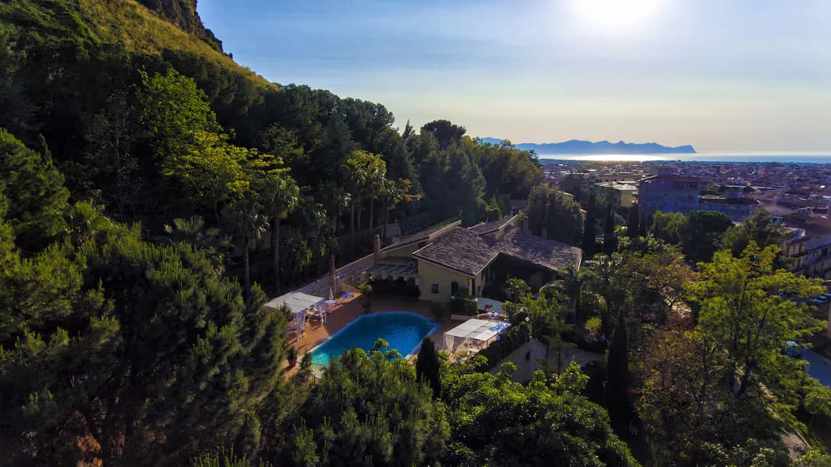 The villa and its pool from above, with the coast beyond the trees